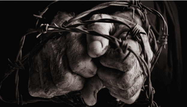 Faded hands clenched in a fist behind barbed wire, symbolizing struggle and resilience. Reflects themes of hardship, perseverance, or social issues, ideal for emotional storytelling or awareness campaigns.