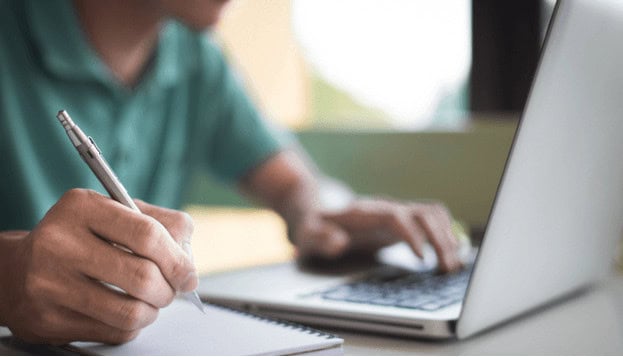 Hands typing on a notebook with a laptop in the background, representing computer training and IT education at MyComputerCareer.