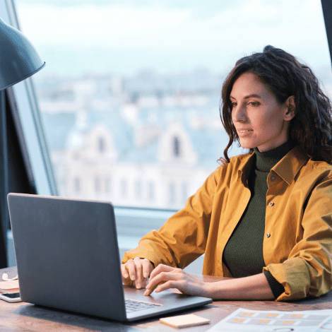 Brightly lit woman working on a laptop in a modern office space, focusing on tech education and computer career training with MyComputerCareer.