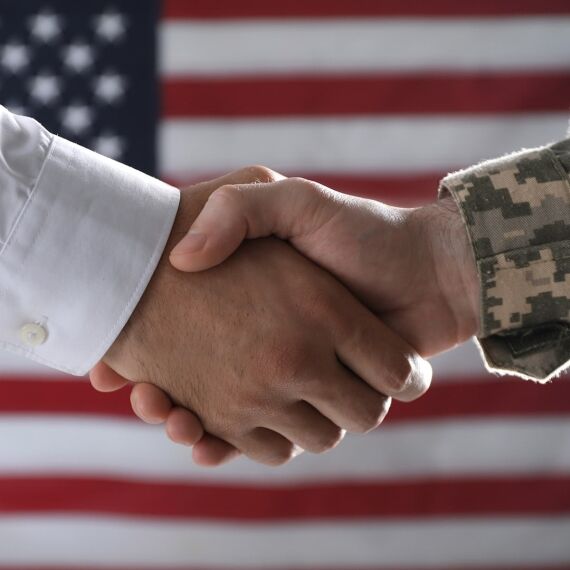Handshake between a person in a white shirt and a person in military uniform with an American flag in the background, symbolizing career readiness, veteran support, and military to civilian career transition.