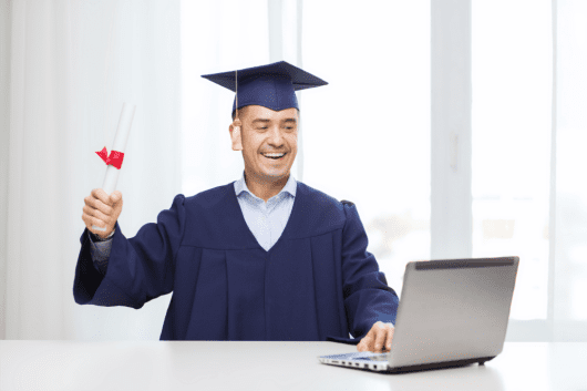 Graduate in computer technology holding diploma, celebrating success at home, with laptop on table.