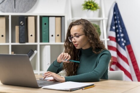 Computer technician woman studying IT certification online, working on a laptop with American flag in background, affiliated with MyComputerCareer, focused on tech career training and IT education.