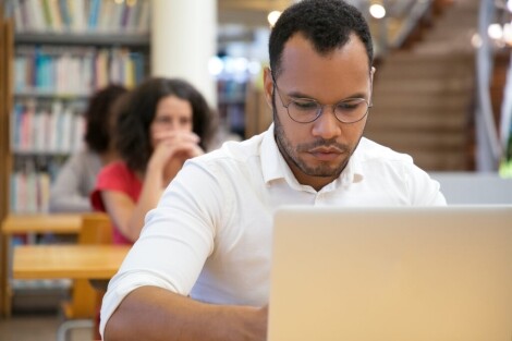 Focused male student using a laptop in a modern classroom, representing online and classroom IT training at MyComputerCareer for career-focused tech education.